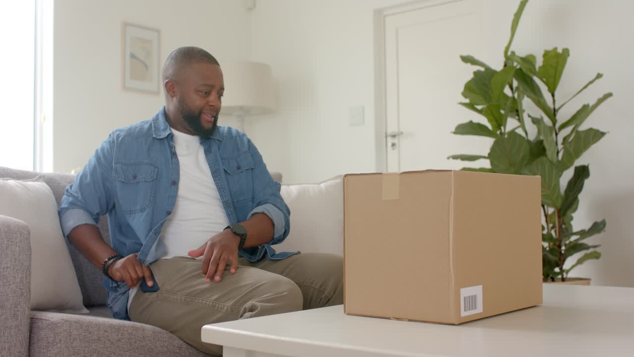 African American man sitting sofa, checking phone after alert, verifying label on box, copy space