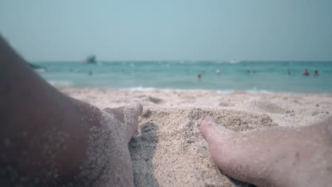 el tipo de la pierna mueve la arena amarilla contra las olas del océano en primer plano