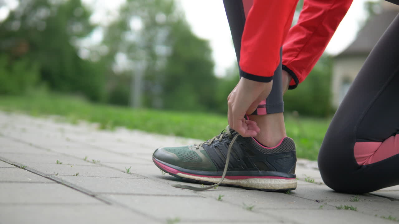 Ripresa da bassa angolazione, donna in abbigliamento sportivo che si allaccia la scarpa preparandosi a correre nel parco.
