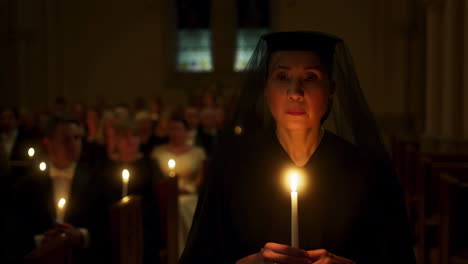 woman in black veil holding a candle at a solemn church service