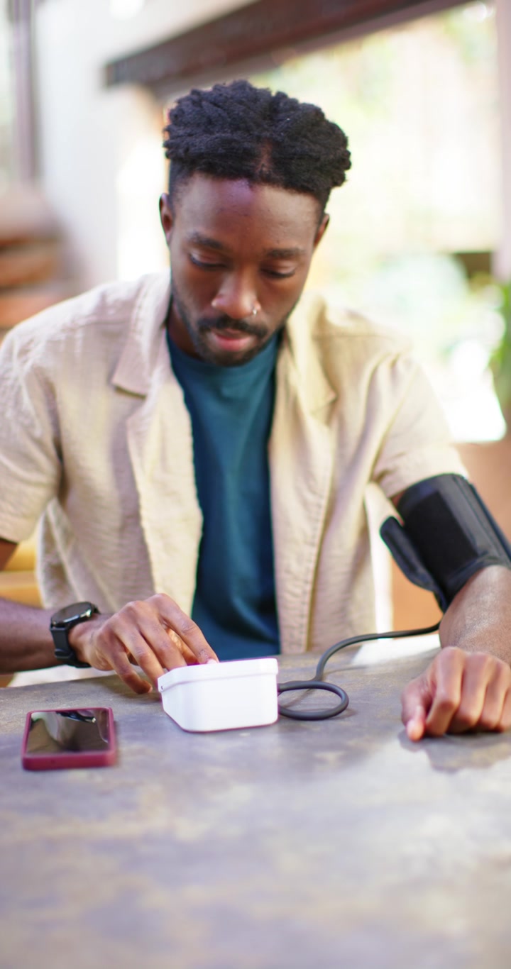 Video verticale: Uomo africano che posiziona il dispositivo, regola il bracciale e controlla la pressione sanguigna con il telefono