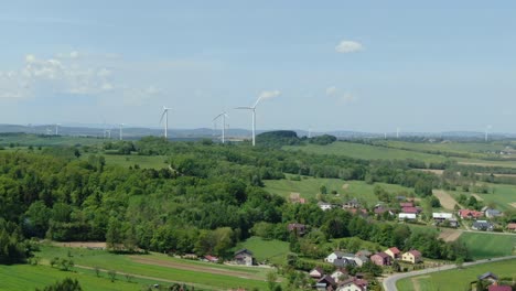 Wind-turbines-spin-large-blades-at-wind-farm-off-in-distance-behind-small-polish-village