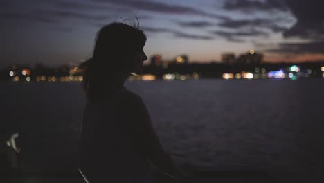 silhouette of a young attractive woman against a background of a night city aboard a boat