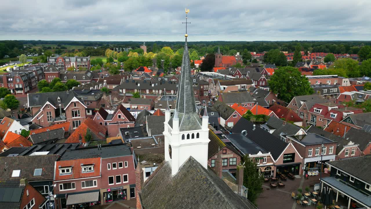 Drone view of Ommen’s white church tower with spire rising above red rooftops, surrounding streets, and outdoor terraces. Location: Ommen, Overijssel, Netherlands (Ommen, Overijssel, Nederland)