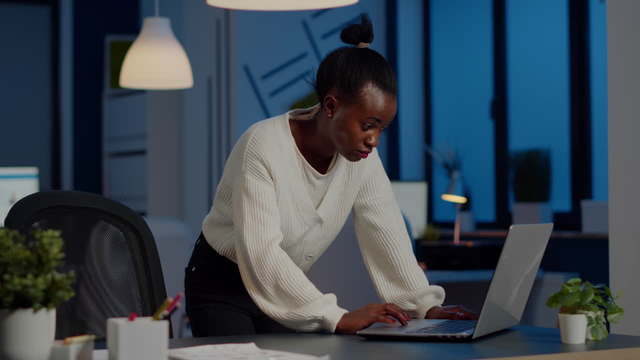 Manager black woman standing at desk searching on laptop and looking at camera