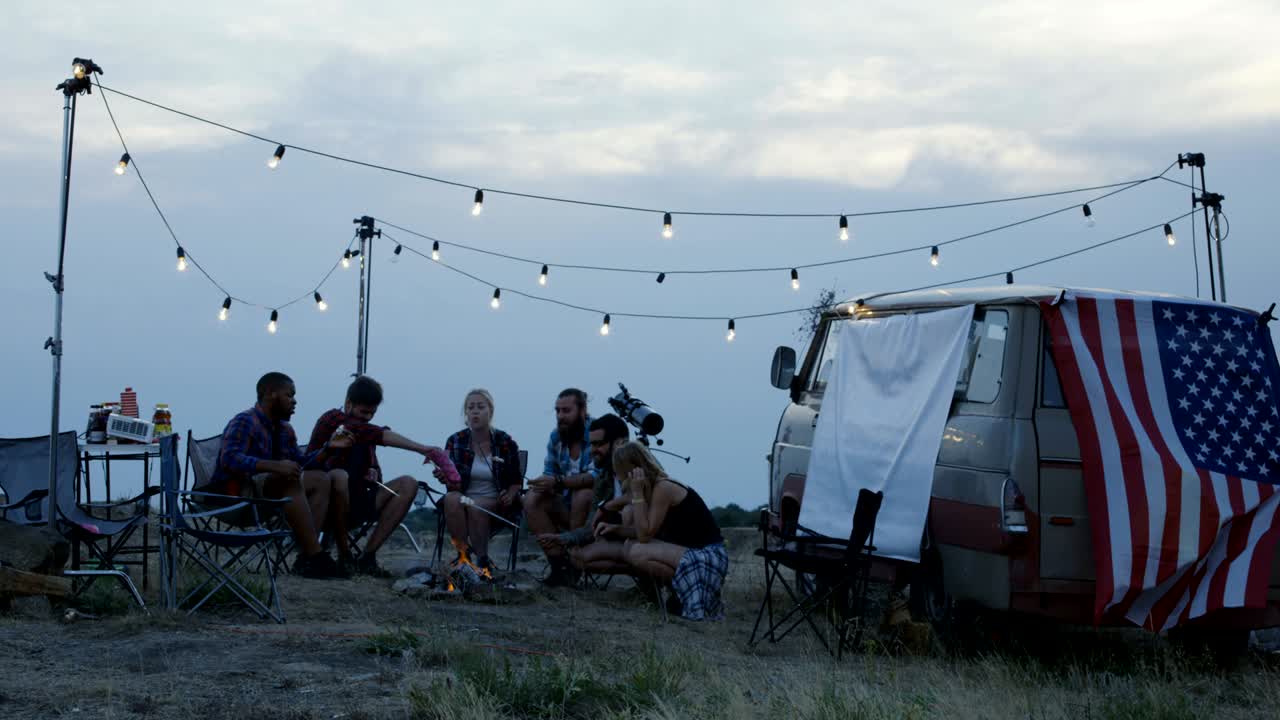 Tourists frying marshmallows at camping bonfire