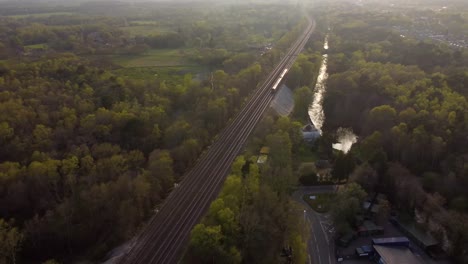 Schöne-Luftaufnahme-Des-Zuges,-Der-Bei-Sonnenuntergang-Mit-Wald-Und-Feldern-Fährt