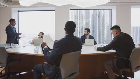 mature businessman standing giving presentation to colleagues sitting around table in modern office