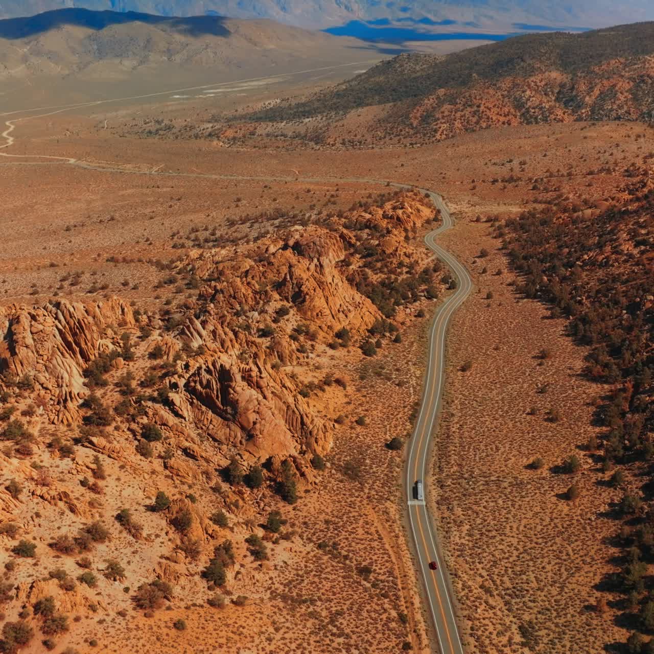 Transport on the highway passing between the craggy mountains. Sunlit panorama of Nevada mountainous landscape on sunny day. Top view