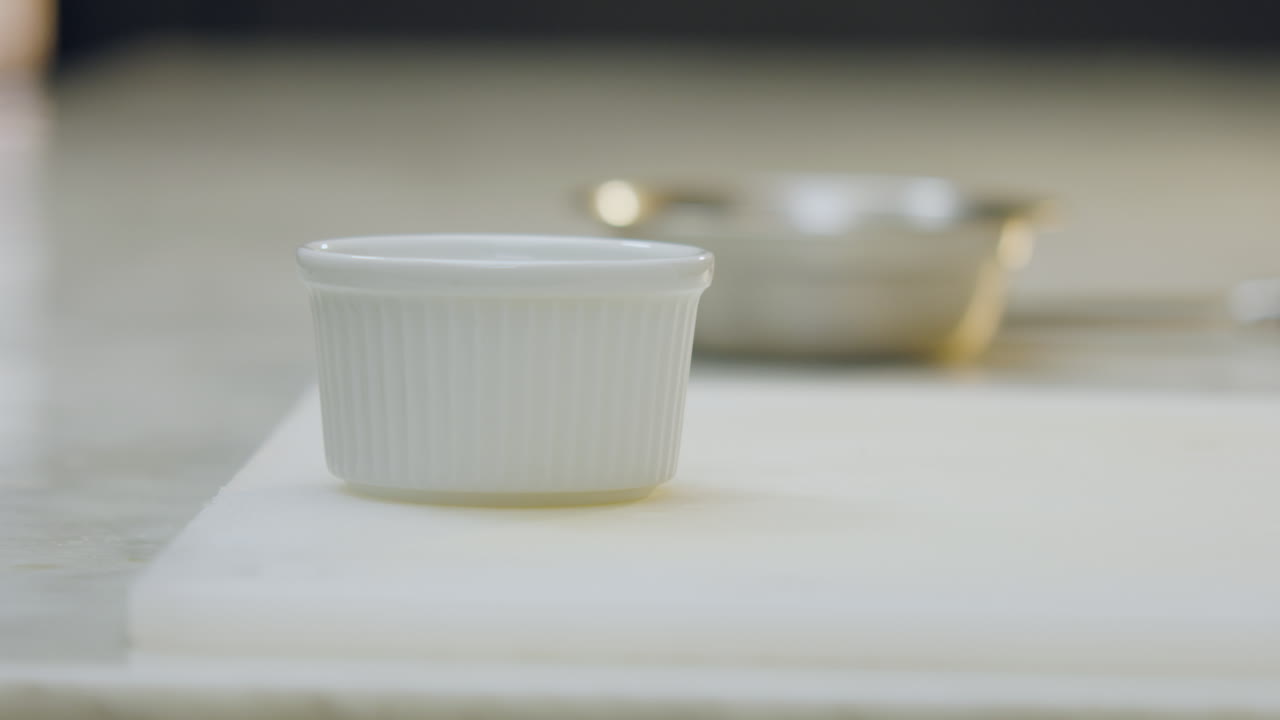 Close-up of a chef placing a ceramic mold on a chopping board. In the background, softly blurred, an aluminum mold can be seen