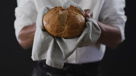 Video-of-cook-holding-loaf-of-bread-on-black-background