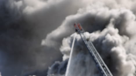 una manguera de incendios en una escalera extendida pulveriza agua sobre un fuego con una nube de humo en el fondo