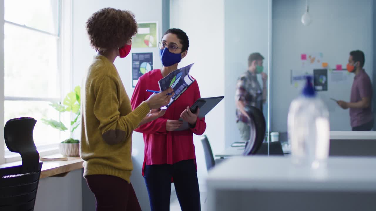 Mixed race female colleagues wearing face masks in office