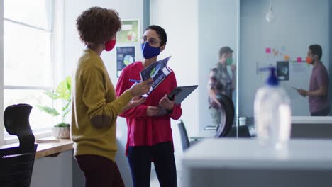 Mixed-race-female-colleagues-wearing-face-masks-in-office