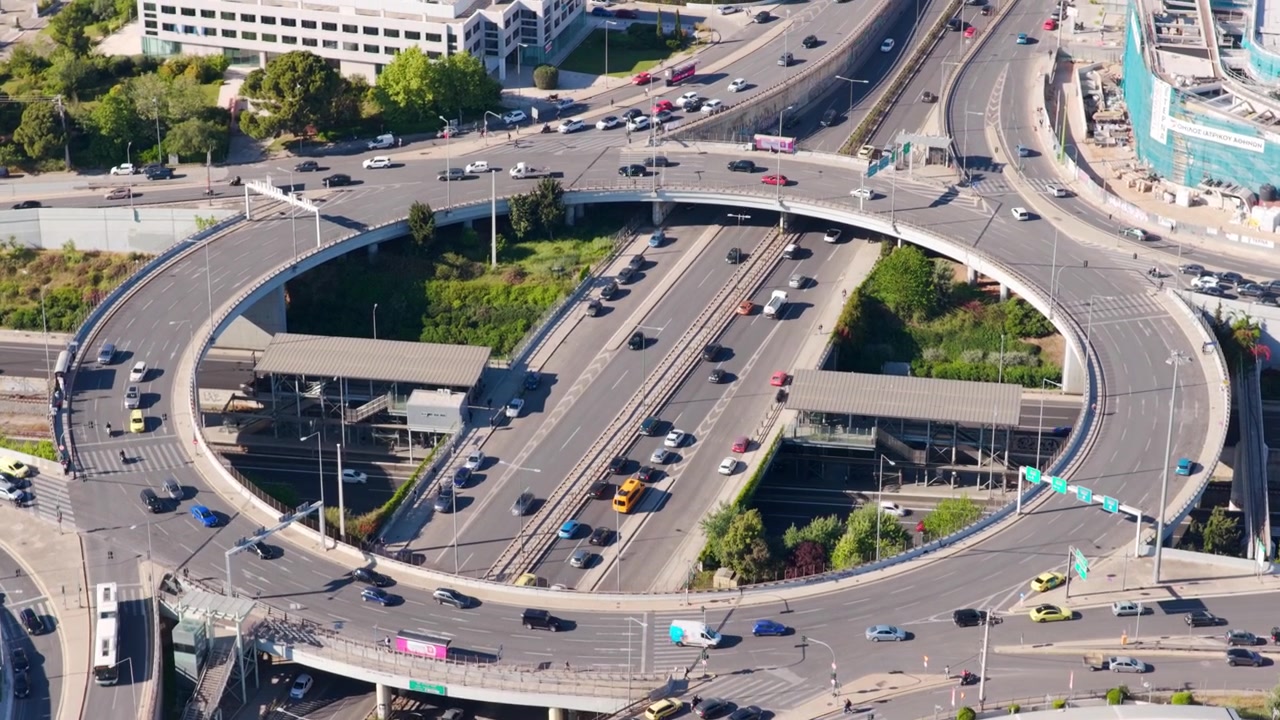 車両が複雑な多層高速道路ジャンクションを移動する賑やかな都市のロータリー。現代の交通インフラと、活気ある都市景観における日々の通勤風景が描かれている。