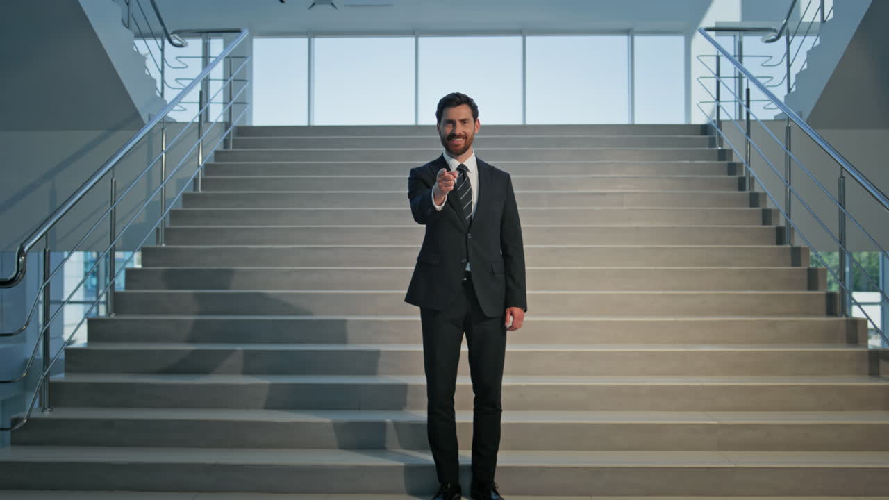 Smiling ceo pointing finger to camera on office stairs. Happy businessman
