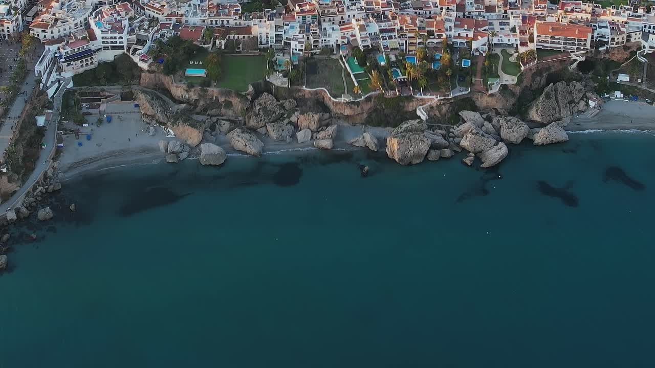 Set oppefra af klippefyldt kyst og turkisblåt hav