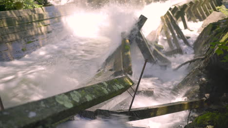 Rushing-Water-Rapids-Running-Through-Log-Chute-and-Crashing-Into-Damaged-Moss-Covered-Log-Chute-Wooden-Beams-During-Golden-Hour-4K-ProRes