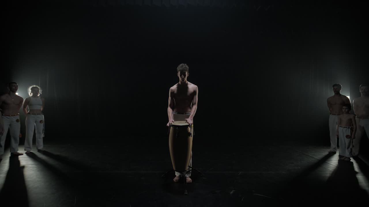un grupo de bailarines profesionales están practicando capoeira en la oscuridad contra un foco de luz en un fondo negro de estudio. arte marcial afro-brasileño que combina elementos de la danza.