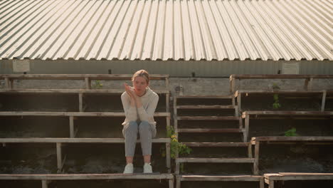 pensive woman in casual attire sits on rustic stadium bleachers, hands joined together, looking downward thoughtfully, she appears deep in reflection