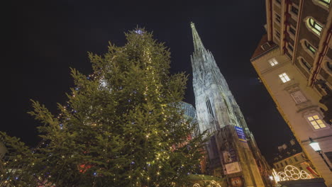 people walk around a tall christmas tree in a city at night