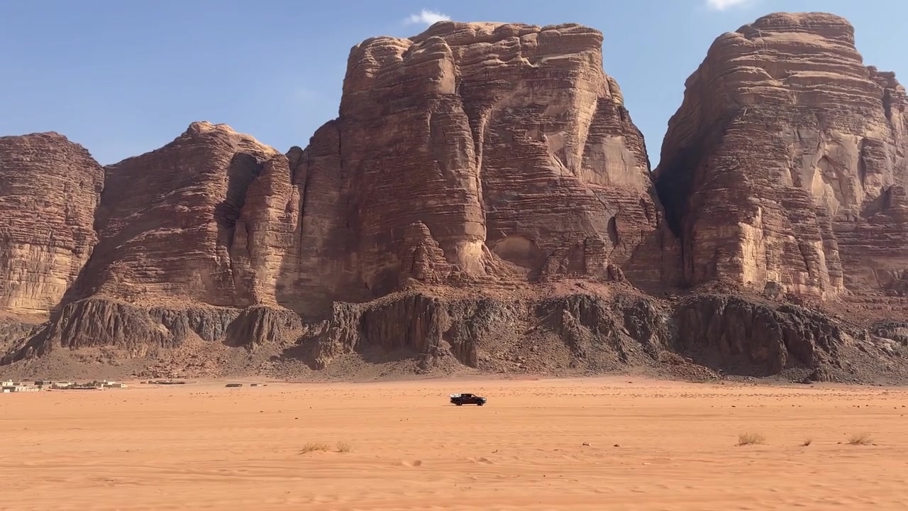 Spændende optagelse af en lastbil, der suser gennem det enorme røde ørkenlandskab i Wadi Rum, indrammet af tårnhøje dramatiske sandstensbjerge i en af Jordans mest ikoniske destinationer.
