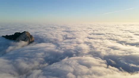 rocky peak rising above a sea of clouds at sunrise with clear blue sky in the background