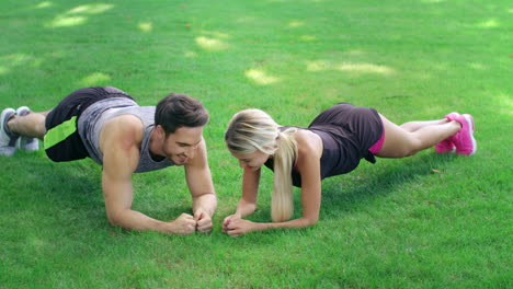 Athlete-man-and-woman-training-together-plank-exercise-on-lawn-in-summer-park.