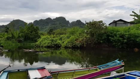 Coloridos-Botes-Pequeños-En-Un-Río-Con-Un-Fondo-De-Colinas-En-Rammang-rammang,-Makassar,-Indonesia