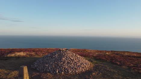 stone cairn at sunrise on cliff above the ocean sea - pushing drone shot 4k uhd