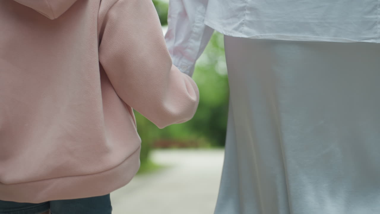 엄마와 딸이 공원을 산책합니다. 부모와 어린 소녀가 평화롭게 손을 잡고 걷습니다. 엄마와 딸은 따뜻한 여름 햇살을 즐기며 그늘진 공원 길을 따라 평화롭게 거닐고 있습니다.
