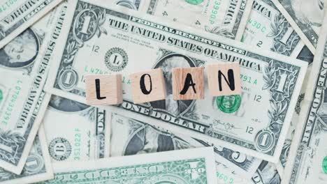 rotating word loan from wooden letters, on dollars, concept