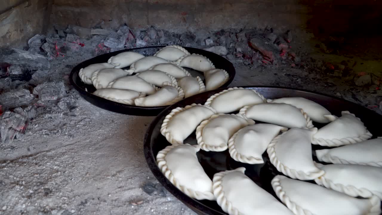 primer plano de dos bandejas de empanadas crudas esperando ser cocinadas dentro de un horno de barro