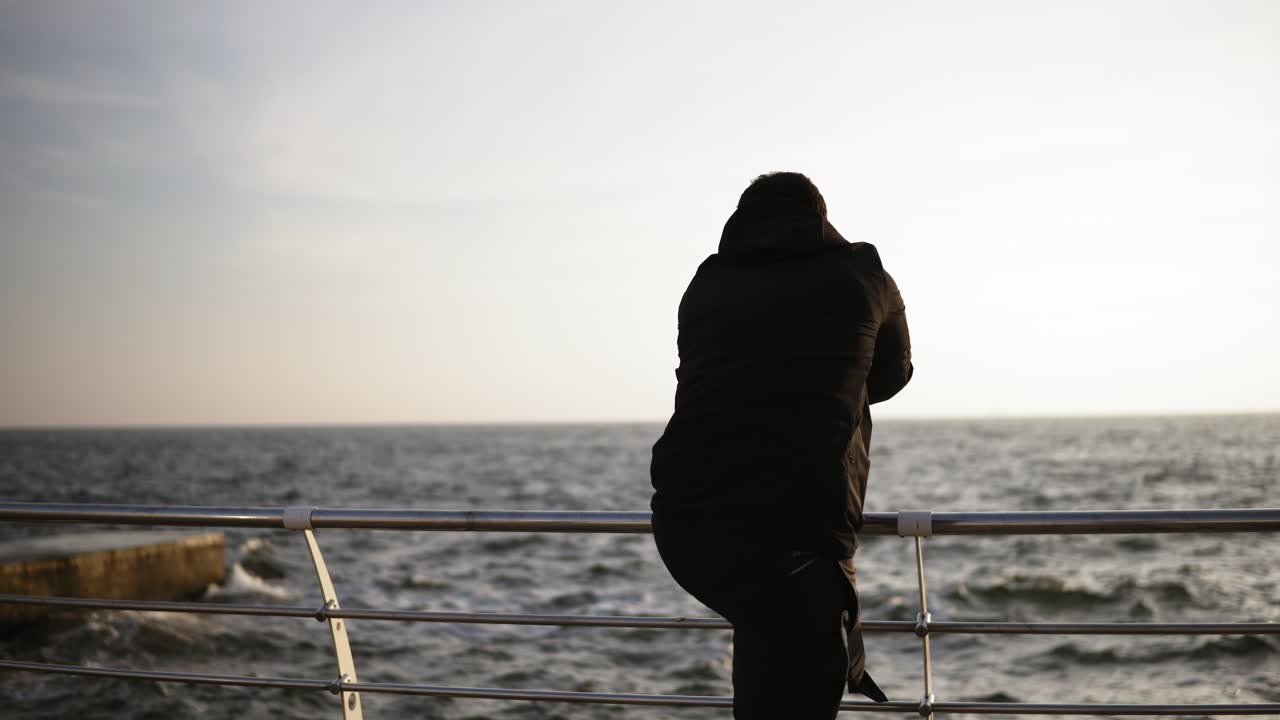 해변 근처의 항구에  ⁇ 어있는 젊은 스포츠 남자. 해변에서 아름다운  ⁇ 빛 아침. 야외 영상.