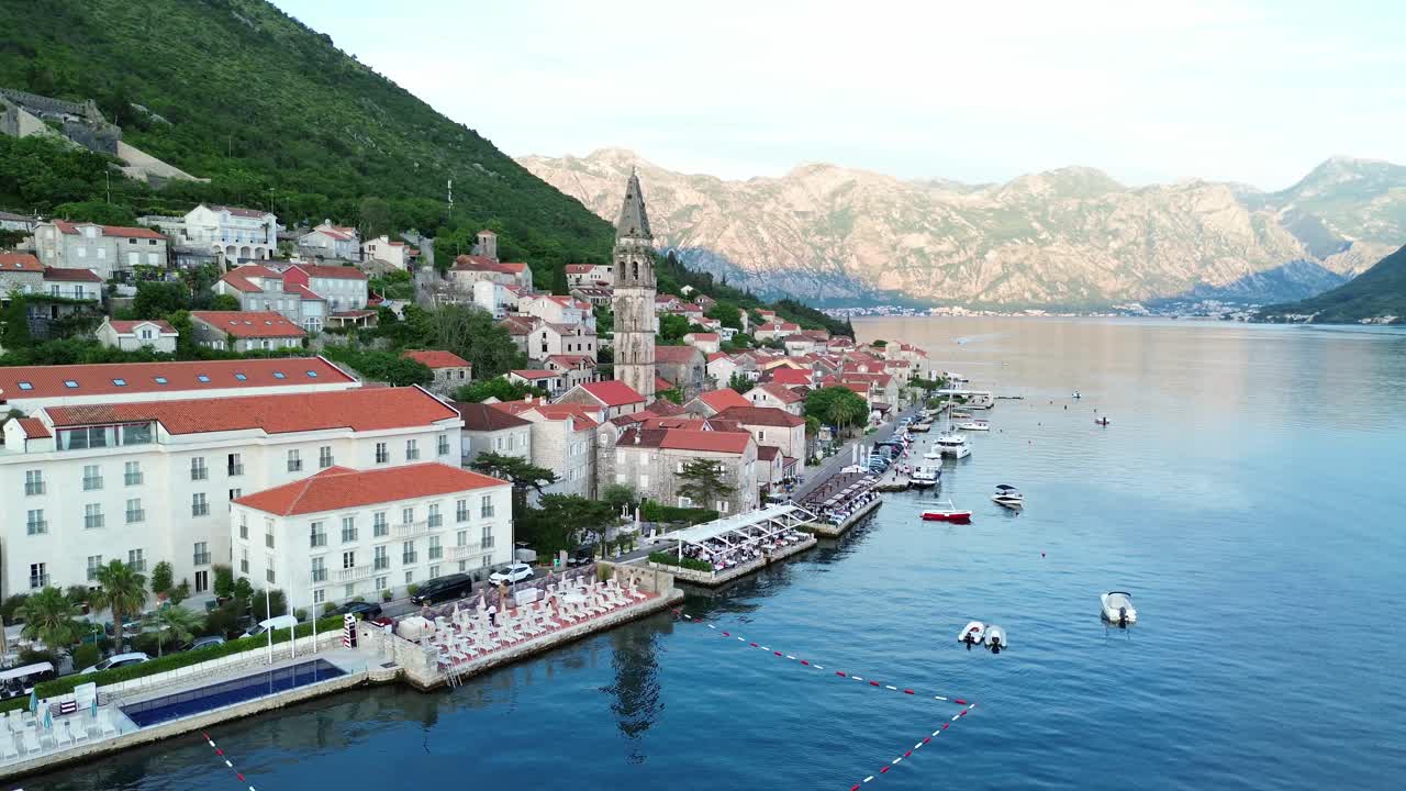 Perast town on bay of Kotor, romantic waterfront restaurant patios, hotels, Saint Nicholas catholic church bell tower in view, Aerial pullback shot