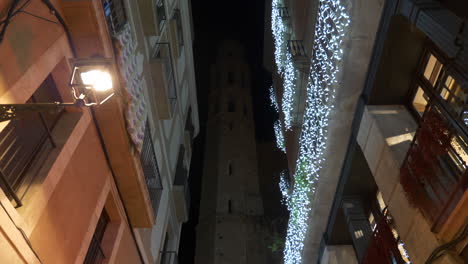 Narrow-street-leading-to-tower-of-Santa-Maria-Cathedral-in-Barcelona-at-night,-dolly-forward