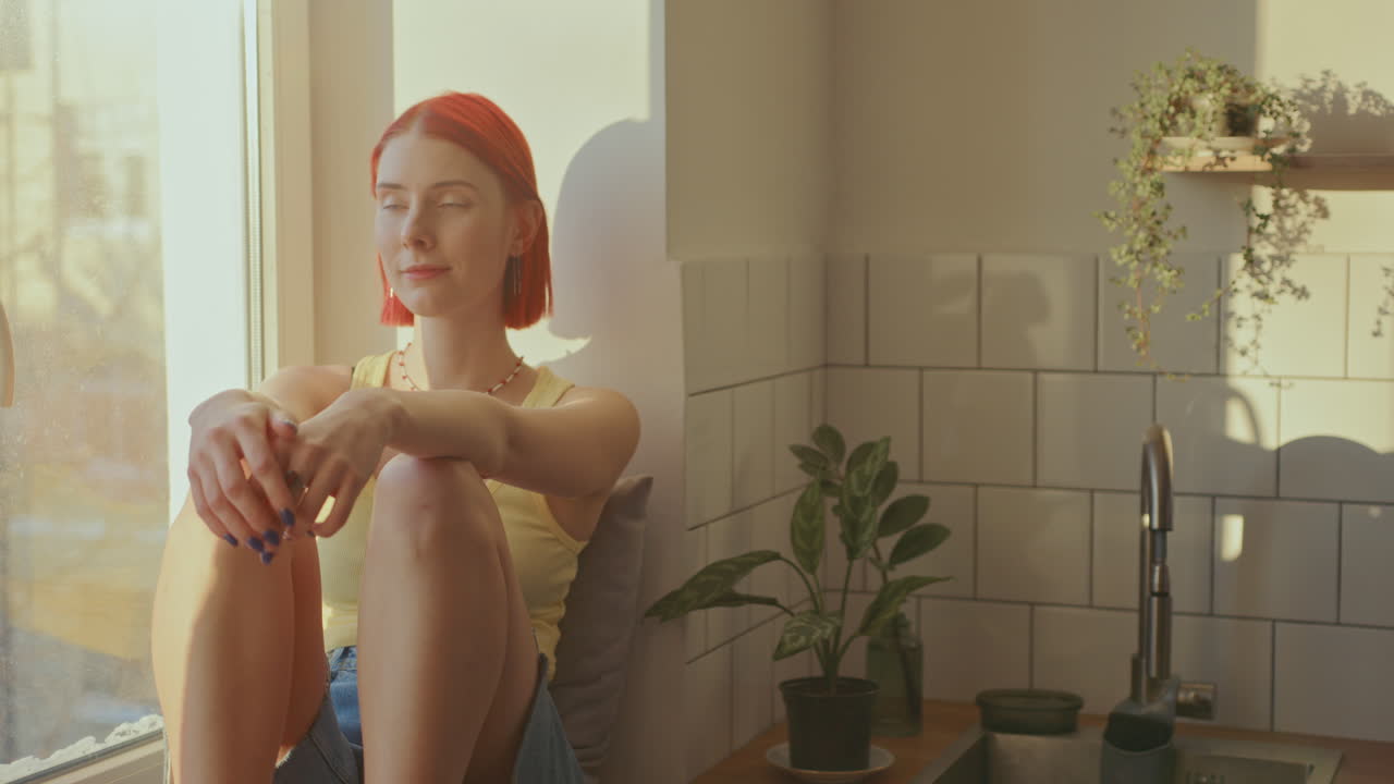 빛 부에서 창문 위에 앉아 있는 예쁜 소녀가 카메라를 쳐다보고 있다