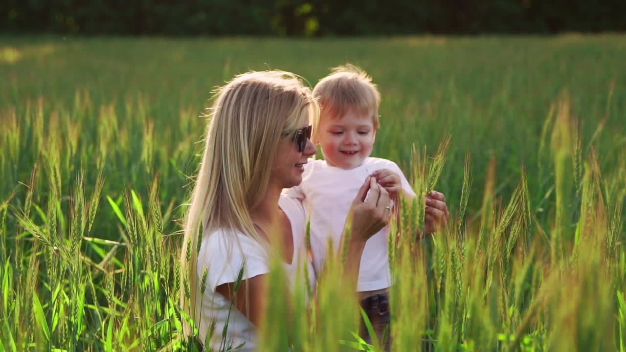 glückliche familie, die spaß hat. babyjunge mit braunen lockigen haaren und seine mutter mit roten haaren, die sich gegenseitig den daumen zeigen. außenaufnahme