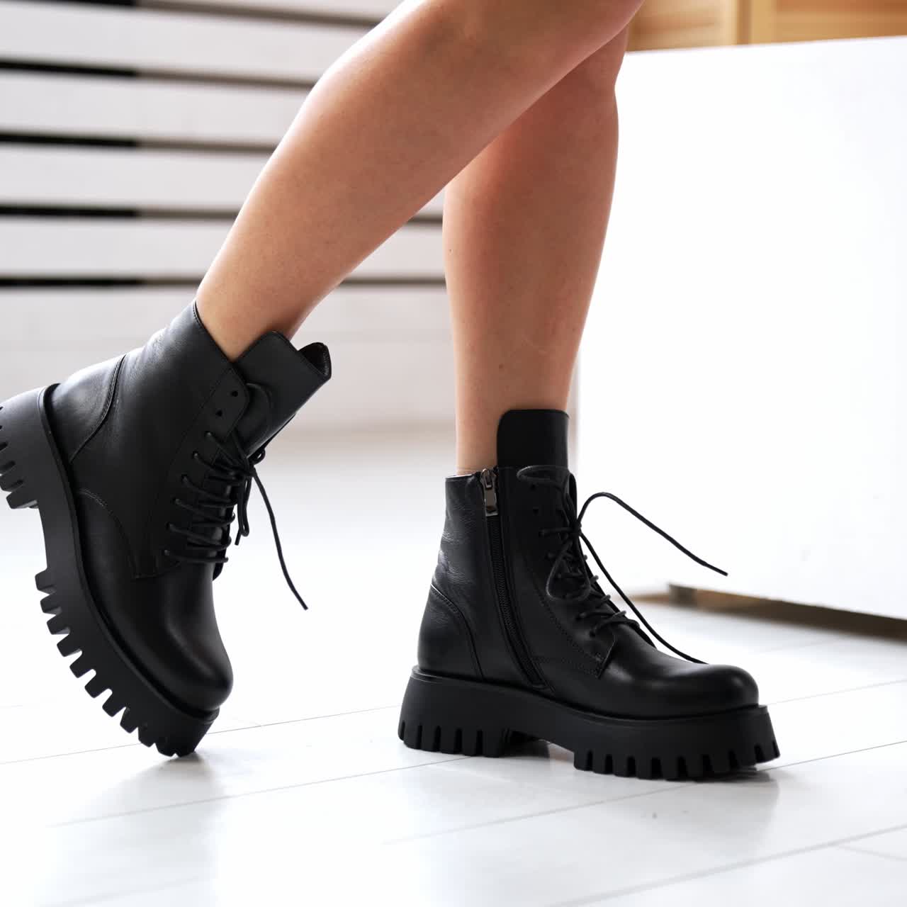 Girl with bare legs and black boots starts to jump. Model demonstrating the stylish leather footwear with laces at white backdrop. Close up