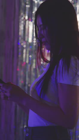 Vertical-Video-Of-Woman-Checking-Messages-On-Mobile-Phone-In-Nightclub-Or-Funfair