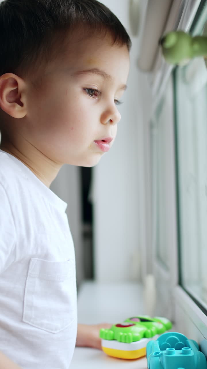 Child looking in window indoor. Sitting lifestyle happy boy. Vertical video