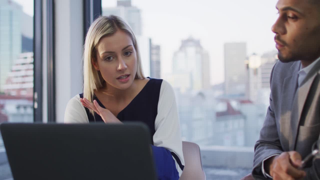 Video of caucasian businesswoman talking to biracial male colleague and using laptop in office