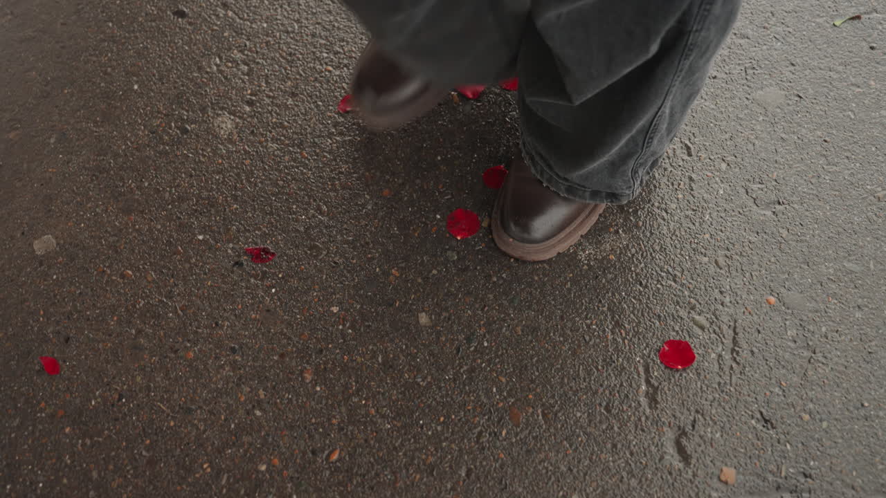 Regennasser Gehweg, übersät mit Rosenblättern und Lederschuhen; ein Künstler arrangiert eine spontane Straßeninstallation; Draufsicht auf reflektierenden Asphalt, mit langsamen, bewussten Schritten und strukturierten Details