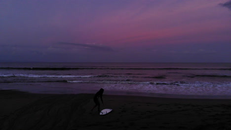 silhouette female surfer getting ready on the beach at sunrise aerial flyover