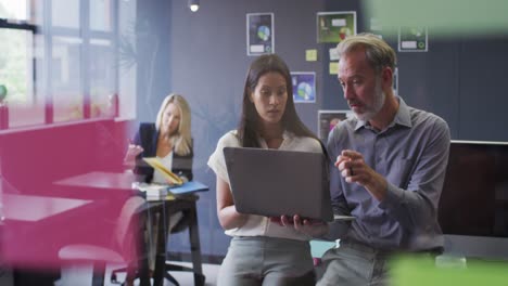 two diverse business people using laptop talking in office and colleague working behind