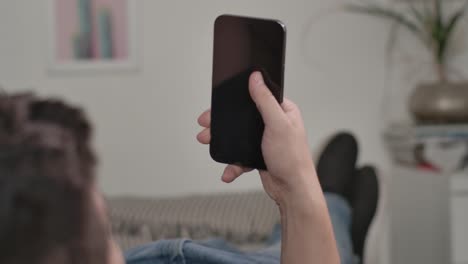 close up shot of man using smartphone device with hand and thumb while laying on sofa couch in office living space