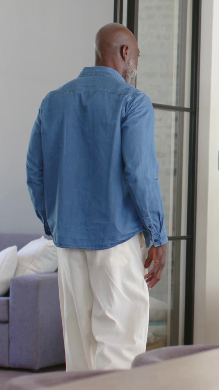 Vertical video: Responding to reach, man turning and entering living room in denim shirt near case