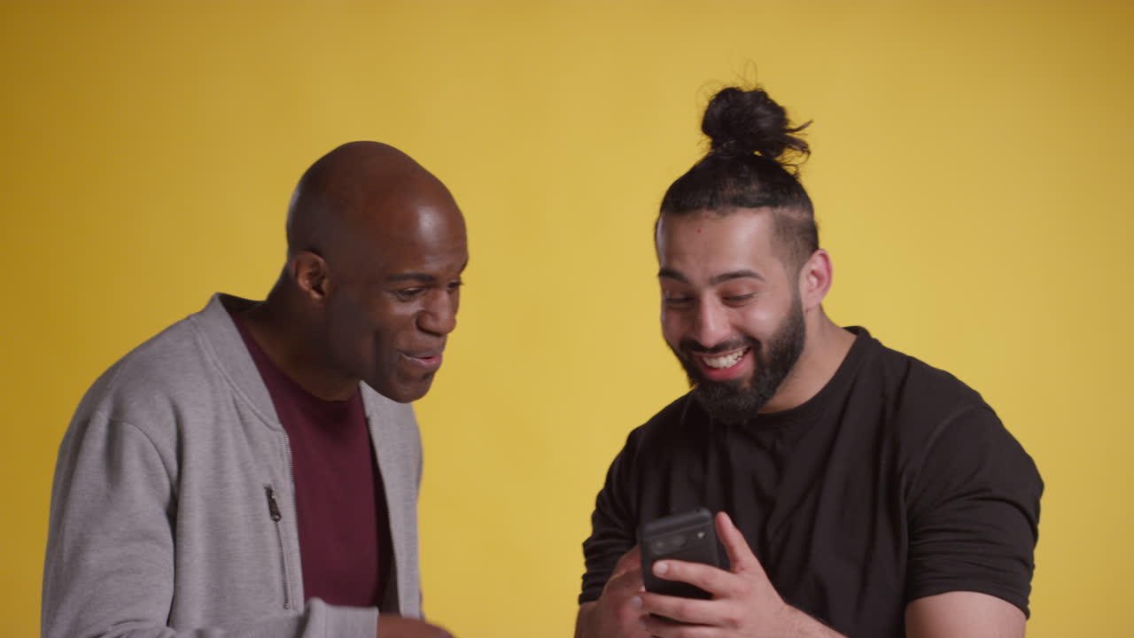 Studio Shot Of Two Excited Male Friends With Mobile Phone Celebrating Winning Money Against Yellow Background 3
