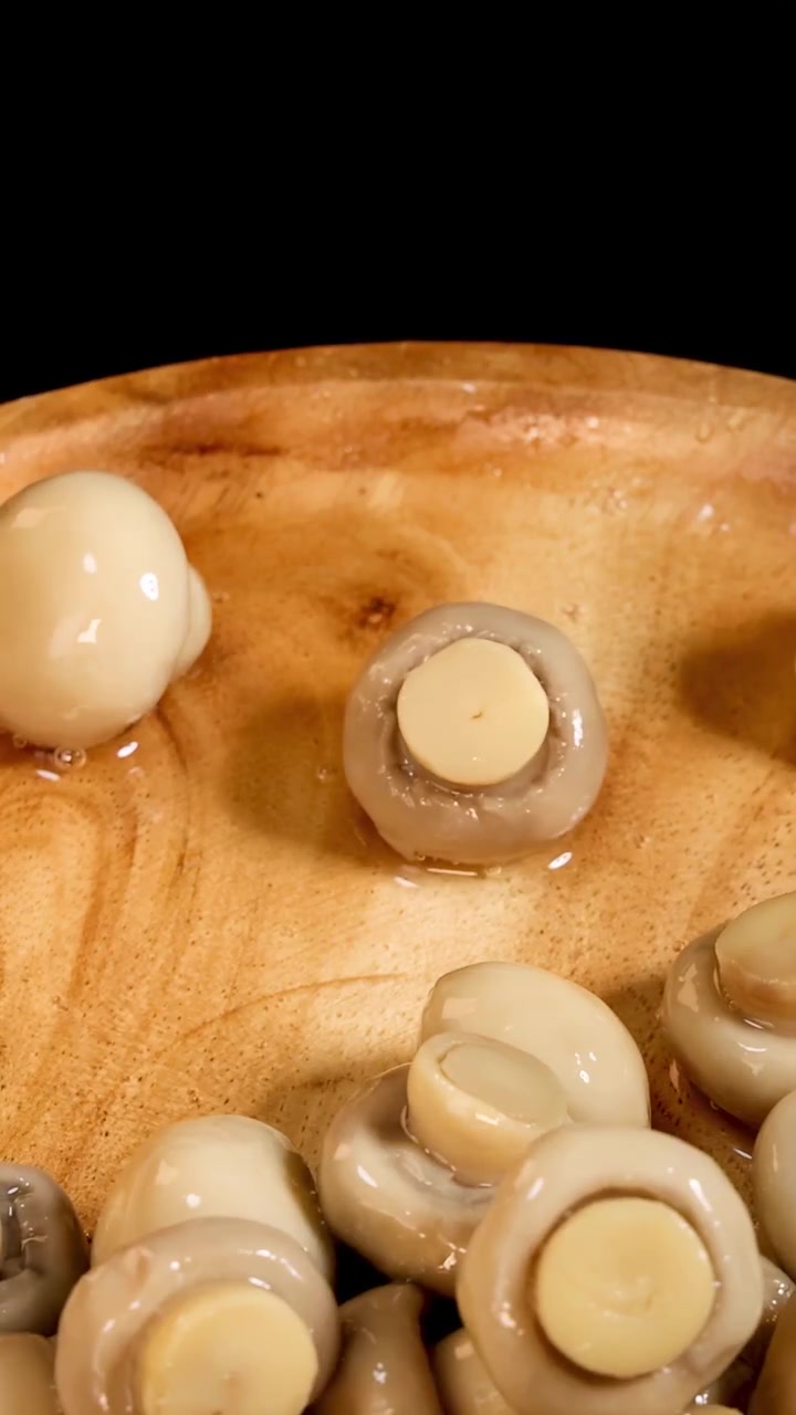 Funghi champignon interi cadono e rimbalzano su un piatto di legno, catturati con una fotocamera ad alta velocità e illuminazione drammatica su uno sfondo nero per una scena culinaria dinamica.