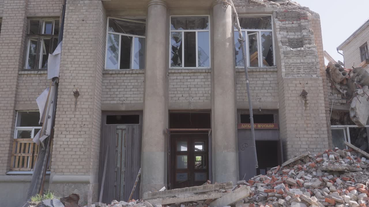 Front view of a heavily damaged school building in shelling with collapsed sections and rubble piles
